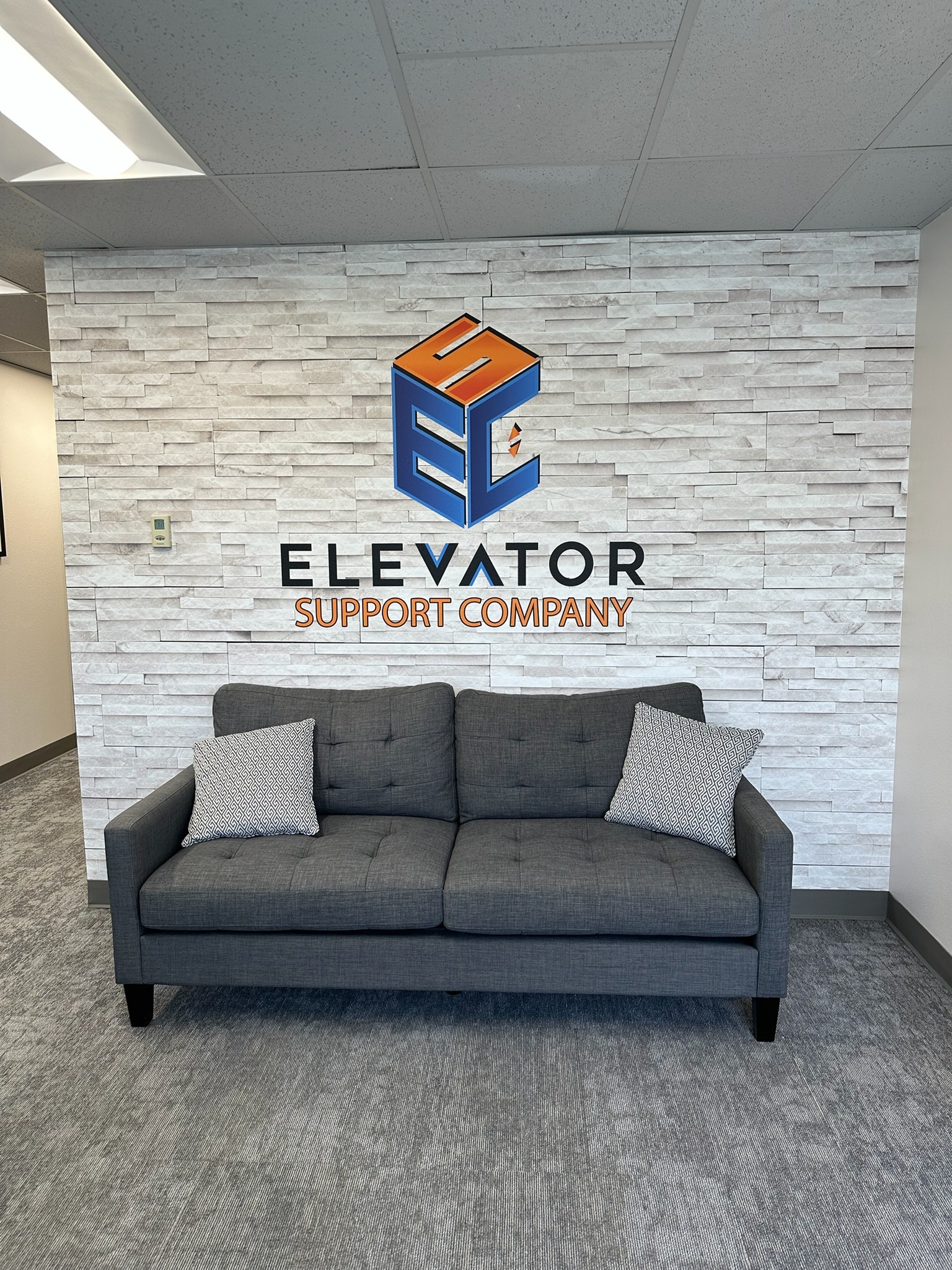 Elevator Support Company logo over stacked-stone print behind a sofa